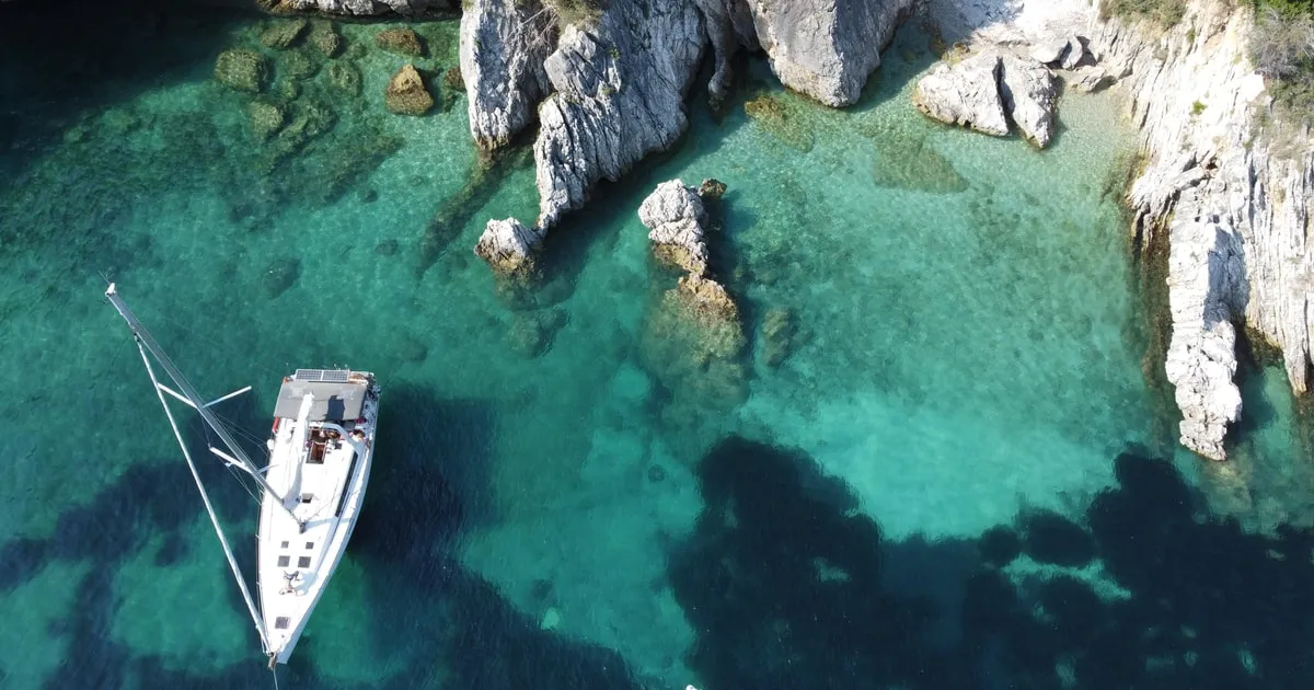 White sailing yacht anchored off Barbati beach under Mount Pantokrator on a Corfu sailing boat tour from Gouvia